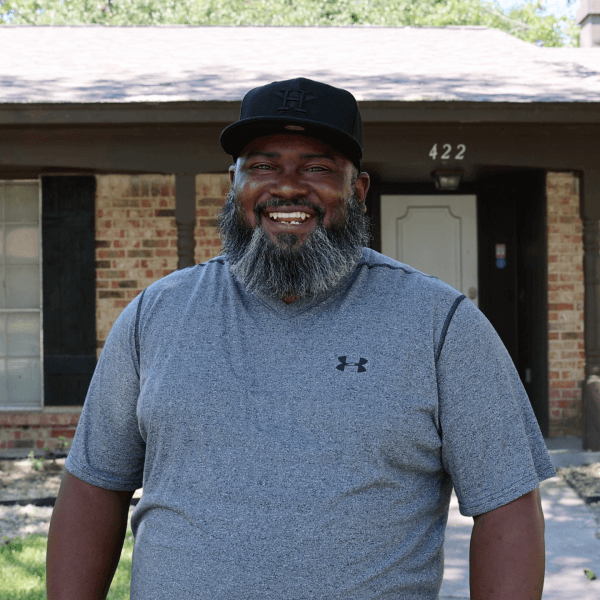 A man with a friendly smile and beard standing in front of his new house, in Texas.