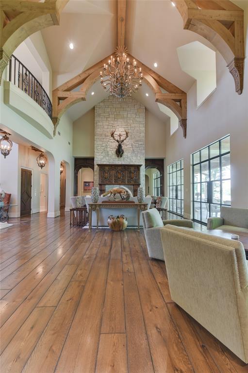 The spacious two story LIVING ROOM (20 X 32) features pitched ceiling with clerestory dormer windows, recessed lighting, decorative wood rafters/carved beam supports, central hanging chandelier, recessed lighting, wide plank hardwood flooring, textured/painted walls, glass/metal doors/glass transoms overlooking patio, over-sized gas log fireplace with carved wood mantle and stone surround.