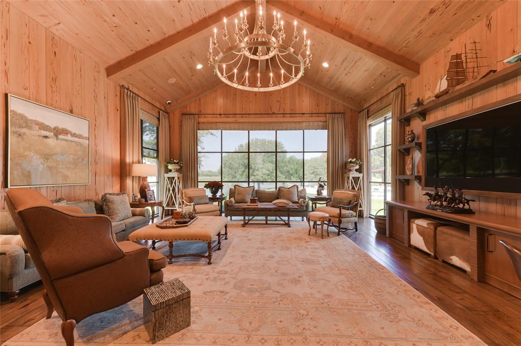 The FAMILY ROOM (25 X 22) is relaxed in design with its 17 foot pitched ceiling (exposed beams/recessed lighting), massive eye-catching round metal chandelier, wood paneled walls, hardwood flooring, built-in TV framed niche with wood shelving, metal-framed windows with custom Roman shades/drapery overlooking to the nearby lake.