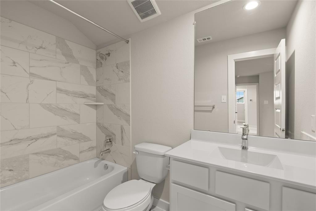 This private bath features tile flooring, bath/shower combo with tile surround, white stained wood cabinets, beautiful light countertops, mirror, dark, sleek fixtures and modern finishes.