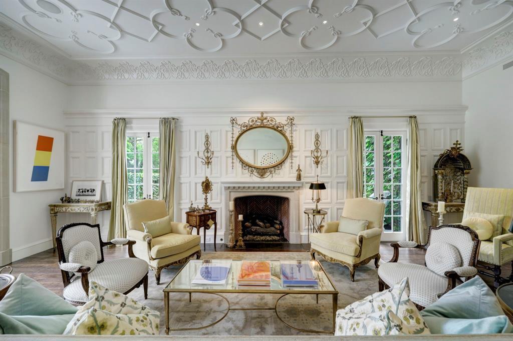 The Formal Living Room with intricate ceiling and crown molding detail. Two sets of French doors flank limestone fireplace and open to the side yard and porch area.