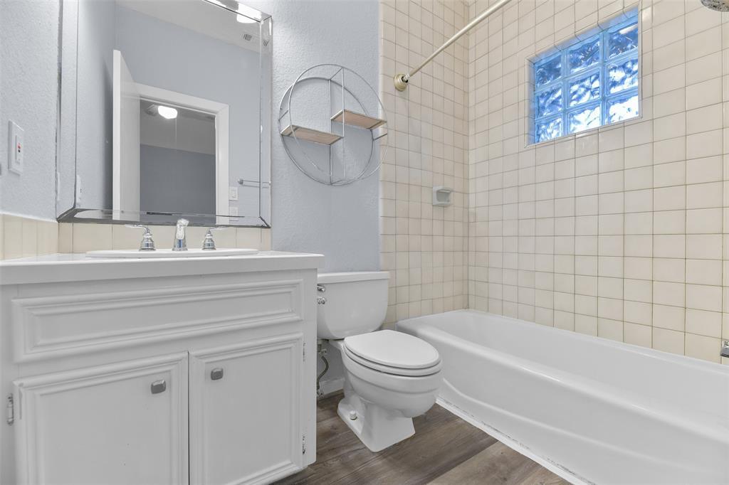 The en suite bathroom in the guest apartment offers a cultured marble countertop with a basin sink, white cabinetry, a beveled frame mirror, luxury vinyl plank floors, and a combination bathtub and shower with a tile surround.