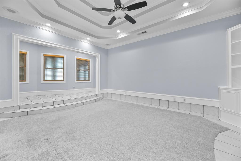 Two steps lead down from the foyer into this sunken living room with plush carpet that was replaced in 2021, a tile border, designer paint, and an impressive triple-trayed ceiling with a lighted ceiling fan, recessed lighting, and built-in speakers.