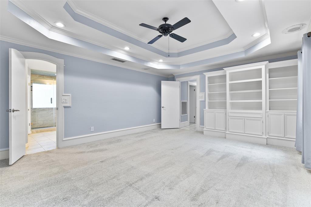 Escape to the privacy of the master suite that boasts a double trayed ceiling with a ceiling fan, recessed lights, custom paint, oversized baseboards, recently replaced carpet, a private patio exit, and a wall of custom built-in cabinetry and shelving.