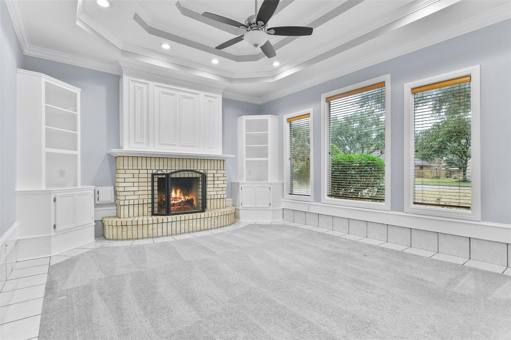 An alternate view of the family room highlights the gas log fireplace with a charming brick surround, custom-built cabinetry above and on either side of the fireplace, and a trio of windows with 2-inch blinds and street-facing views.