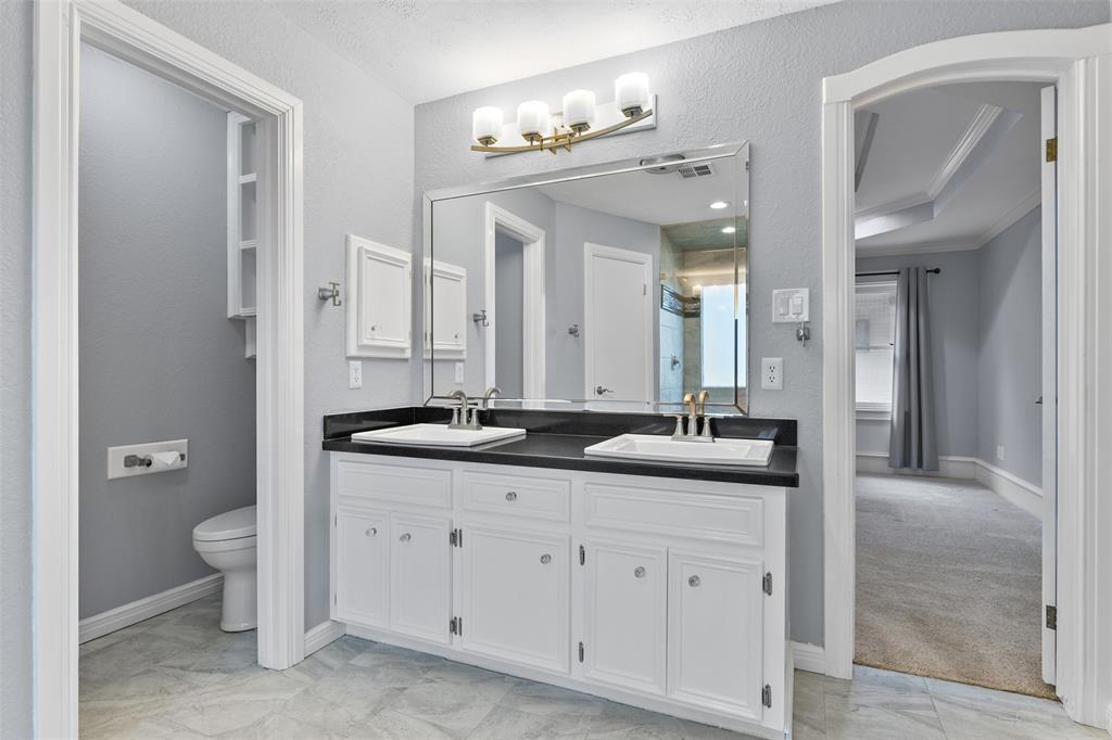 The en suite master bathroom has been masterfully renovated to include a sleek granite top vanity with dual rectangular basin sinks, white cabinetry, designer lighting, tile floors, his & hers closets, and an extra-large walk-in shower with a seamless glass door and a stylish tile surround.