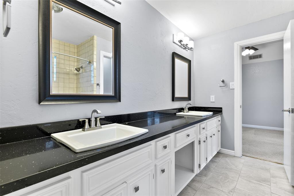 The secondary bedrooms are serviced by Jack & Jill style bathroom with a lengthy black granite vanity with dual rectangular basin sinks, ample white cabinetry, framed mirrors, stylish lighting, and a combination bathtub and shower with a tile surround.
