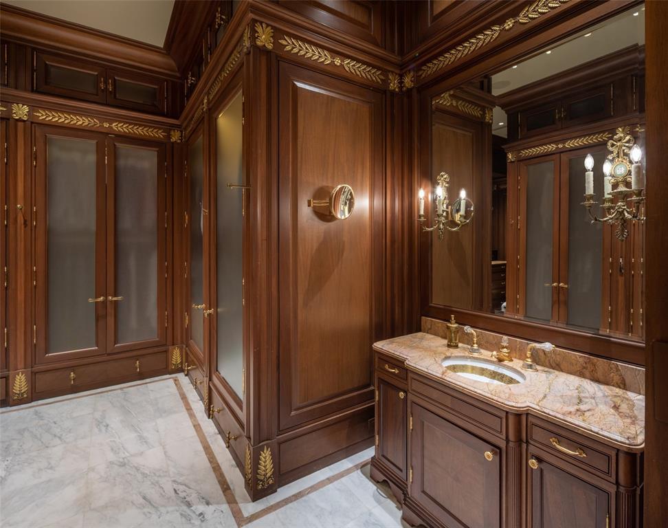 The second Primary Suite walk-in closet features mahogany cabinetry, marble vanity, white inlaid marble floors, ornate lighting, customizable belt, tie and shoe storage, pull-down hanging bars and more.