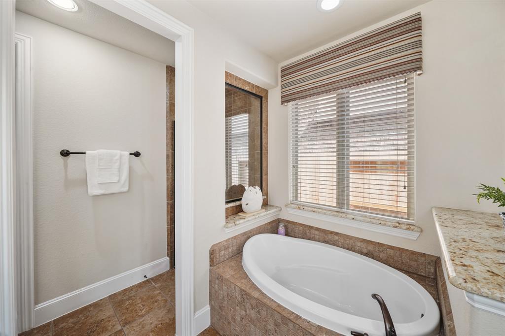 Relax & unwind in the tile surrounded garden tub with window & blinds above along with a tile framed window overlooking the shower area.