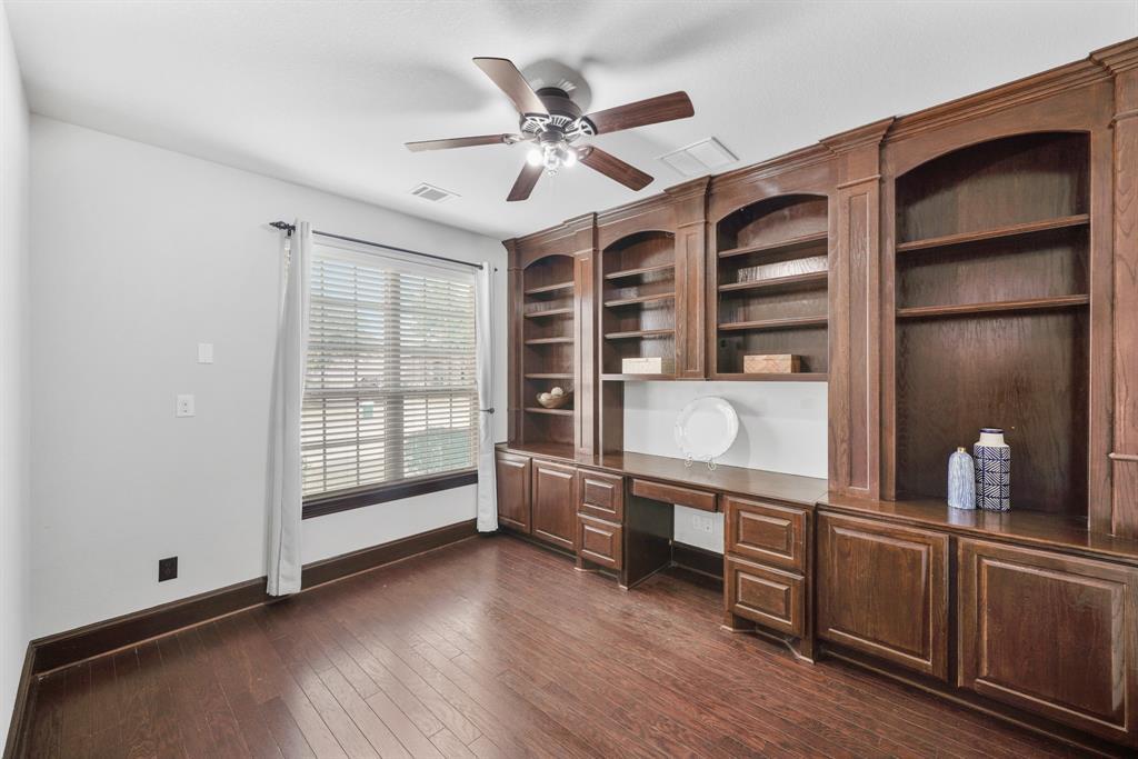 Opposite the formal dining room, the private study has a ceiling fan with lighting, windows with blinds & drapes overlooking the front yard & hardwood floors. Included is a custom wood-stained built-in complete with arched bookcase & display shelves and built-in desk with drawer & cabinet storage below.