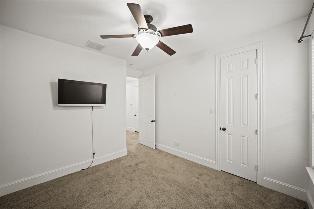 Features include a ceiling fan with light fixture, window with blinds overlooking the side yard, a wall mounted flat screen TV, walk-in wardrobe closet & carpet. The home's second full bath is located nearby.