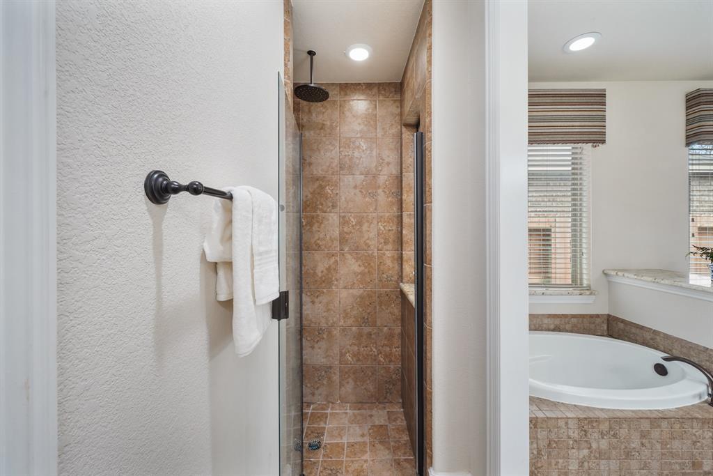 The floor-to-ceiling tile surrounded & glass enclosed shower includes recessed lighting along with ceiling & wall mounted shower heads.