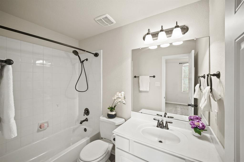 The en-suite bath includes white painted cabinetry, counter top with integrated back splash & sink, wall mounted mirror & lighting, a ceramic tile surrounded combination tub/shower & tile flooring.