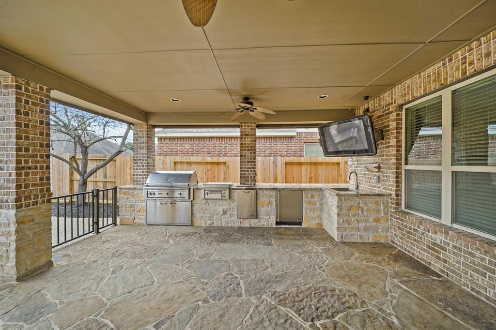 The covered patio includes an outdoor kitchen with stone accents, granite counter top & stainless steel under-mount sink. Appliances include a stainless steel barbecue grill & two-burner gas cooktop by Lynx, a built-in refrigerator and pull-out stainless steel trash bin. The wall mounted flat screen TV stays with the home.