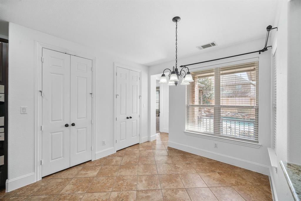 Situated at the end of the kitchen with two double-door storage pantries is a bright & cheery breakfast room with chandelier lighting and surrounded by windows with blinds overlooking the pool with tile flooring. The vestibule in the background leads to the private owner's suite.