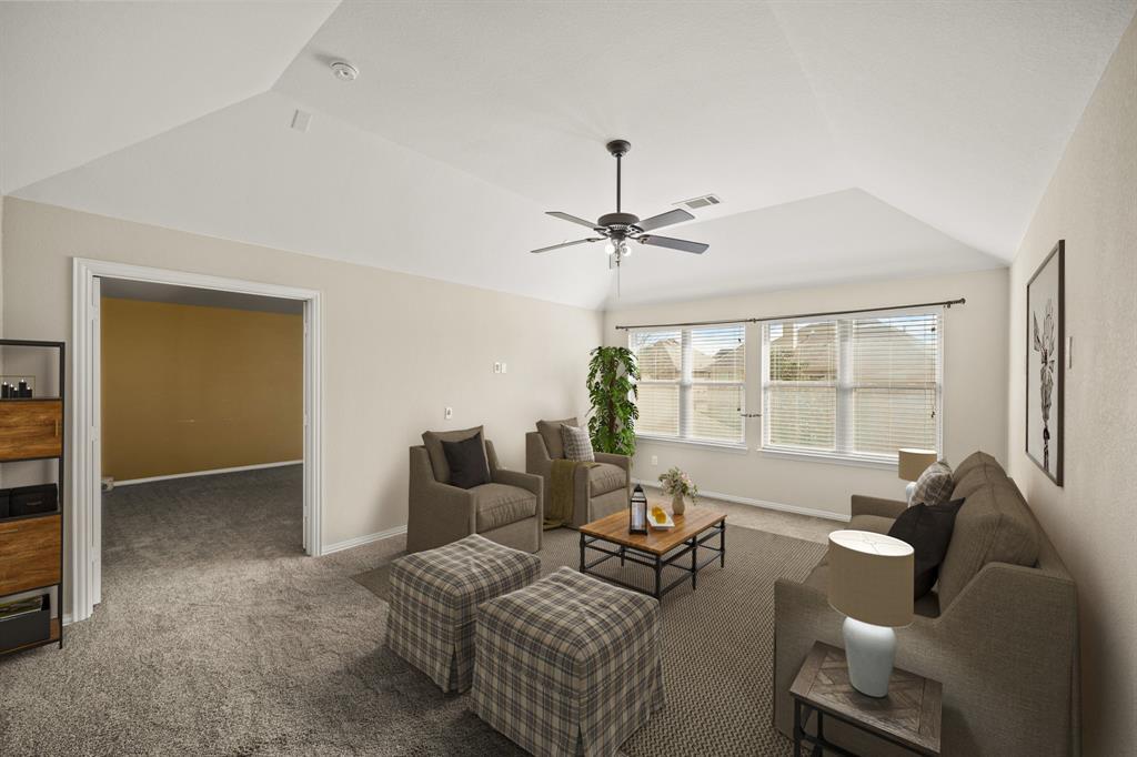 The second floor has as a game room with high ceiling, ceiling fan with lighting, a wall of windows with blinds overlooking the backyard & carpet. A separate media room is shown in the background. This photo has been virtually staged.