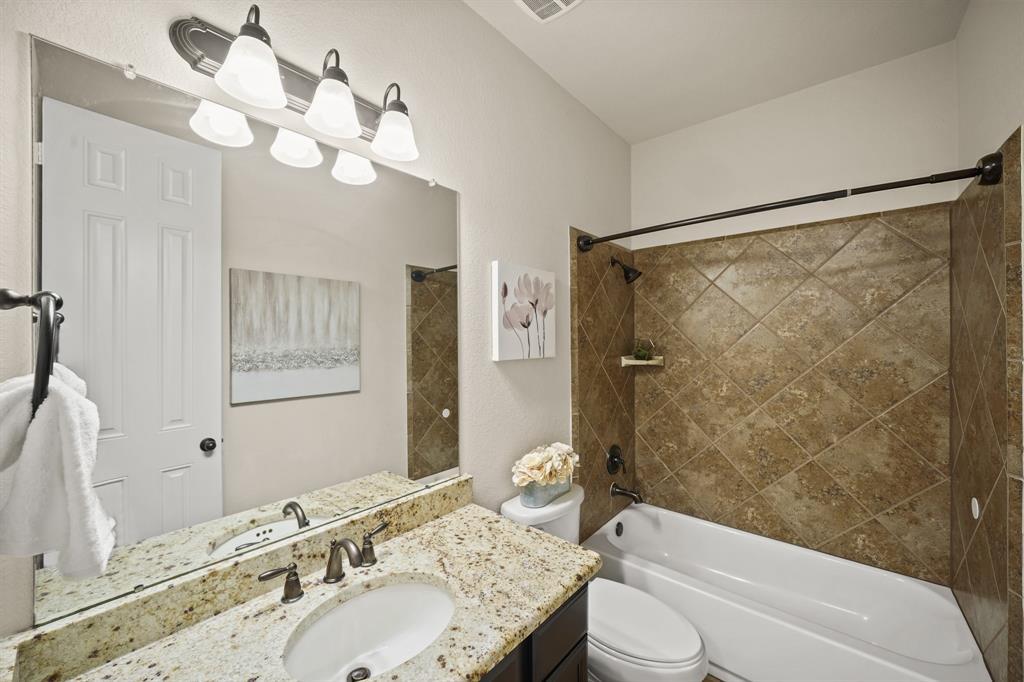 Convenient for guests, the second full bath has wood-stained cabinetry with a granite counter top & integrated back splash, wall mounted mirror & lighting, a diagonally-laid ceramic tile surrounded combination tub/shower with soap/shampoo storage shelf & tile flooring.