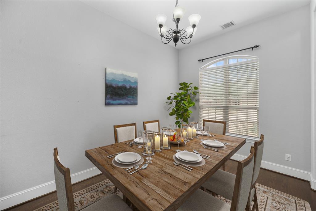 The formal dining with high ceiling, chandelier lighting and an arched window with blinds overlooking the front yard has gleaming hardwood floors. This photo has been virtually staged.