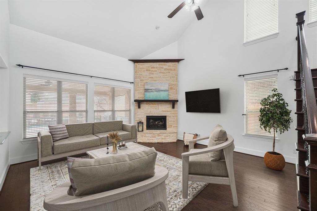 Located on the back of the home with a soaring two-story ceiling, the living room surrounded by windows with blinds includes a ceiling fan with lighting, pre-wiring and mount for a wall mounted flat screen TV & hardwood flooring. This photo has been virtually staged.
