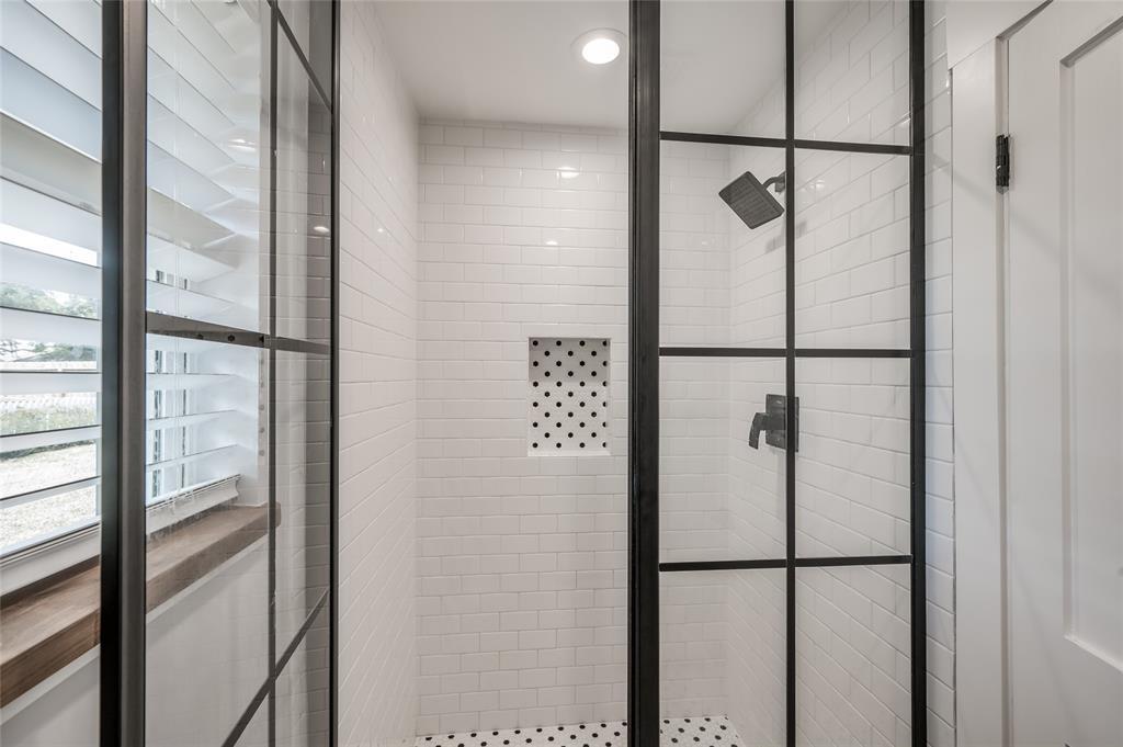 Industrial vibe metal and glass shower doors open to the white subway tile walk-in shower with rain showerhead and shampoo niche.