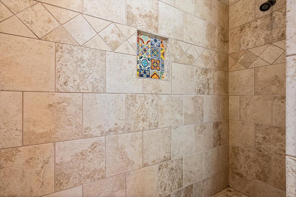 A stone standalone shower is oversized and features decorative stone tile with colorful tile accent.