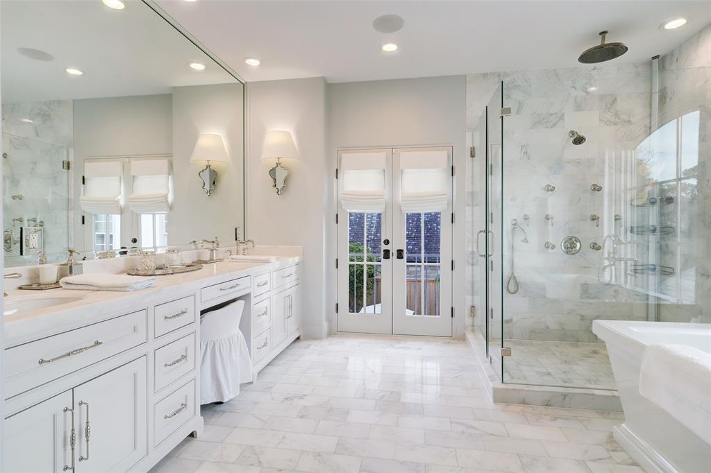 Glamorous primary bathroom with sleek counters and finishes throughout. Gorgeous cabinetry, vanity seat, custom window coverings, frameless shower and separate soaking tub.