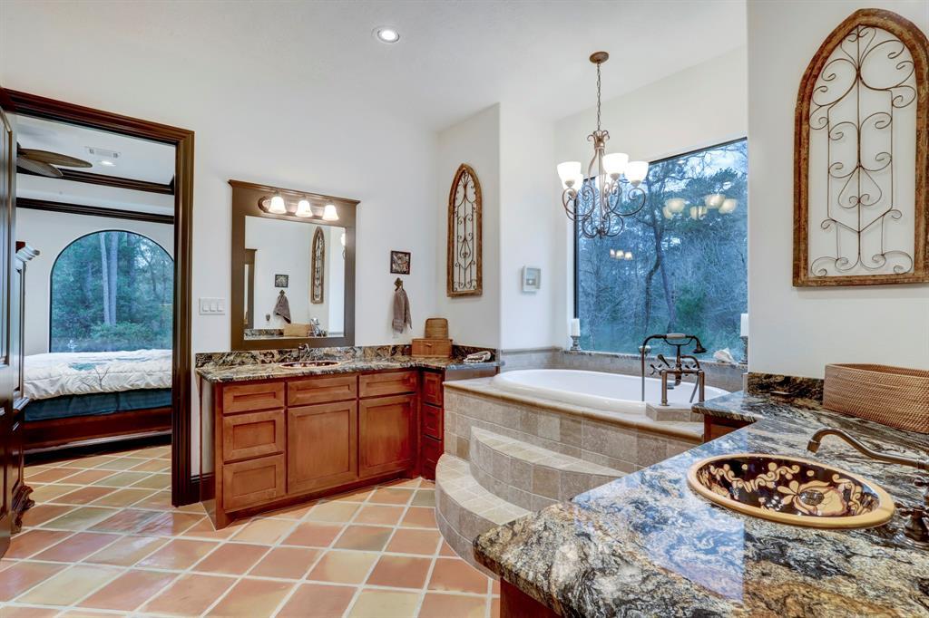 Luxuriate in this elegantly appointed bathroom, where a large window pours natural light onto a sumptuous garden tub. The room features tasteful granite countertops, dual sinks set in rich wooden vanities, and terracotta tiled flooring, all designed to create a spa-like atmosphere of comfort and relaxation.
