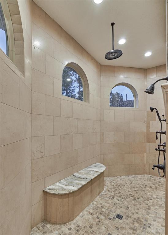 This is the primary ensuite's walk-through shower with dual showerheads and a convenient sitting bench. The arched windows allow an abundance of natural light while still providing privacy.