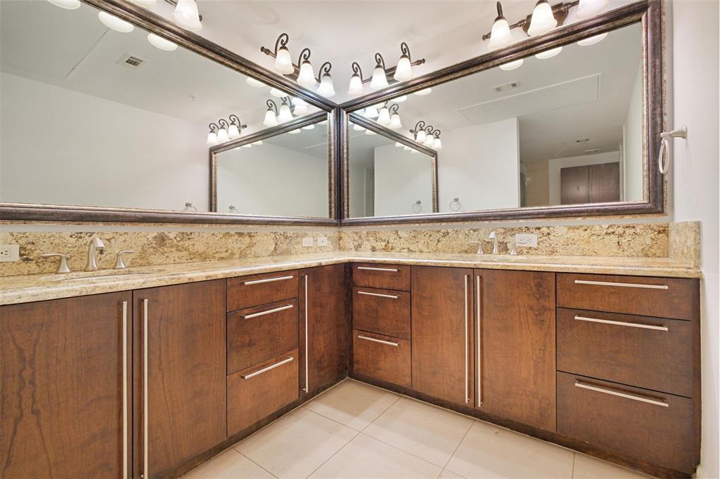Custom cabinetry, granite counters, framed mirrors, and travertine floors add sophistication to the primary bath.