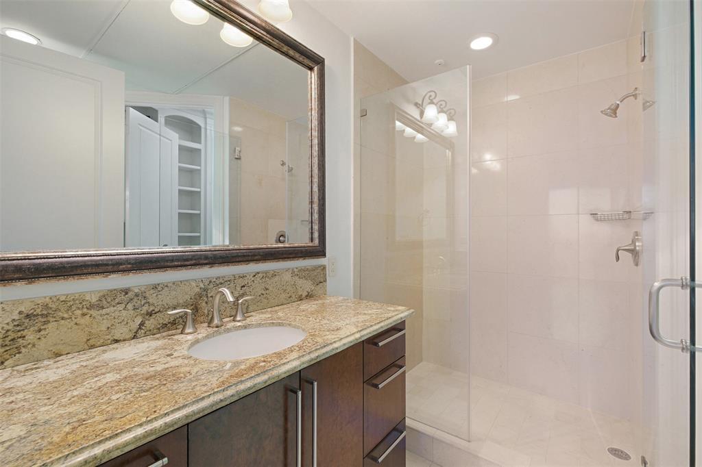 The guest bathroom provides ample storage, custom cabinets, and a frameless glass shower.
